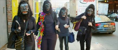 Four members of the Guerrilla Girls are depicted wearing their characteristic gorilla masks as they go on a sticker walk