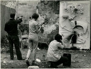 Jean Tinguely (far left) Niki de Saint Phalle, and unidentified man, shooting paint at a nearly finished work (1961). Photo by Shunk-Kender