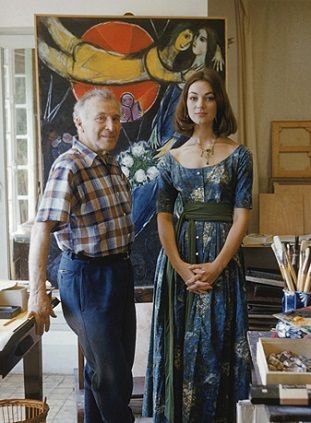 Marc Chagall with model Ivy Nicholson (she wears a dress by Claire McCardell) against Chagall's painting <i>Le Soleil Rouge</i> in his studio in Vence, France (1955)