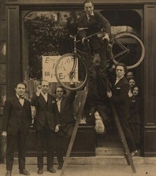 Opening of the Ernst exhibition at the gallery Au Sans Pareil, Paris (1921). From left: René Hilsum, Benjamin Péret, Serge Charchoune, Philippe Soupault on top of the ladder, Jacques Rigaut (upside down), and André Breton