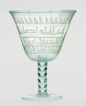 This Islamic goblet (probably from Iraq or Syria), from around the eighth-ninth century AD, features (somewhat crude) scratch-engraved details, including three bands of patterned designs, and one band with a Kufic calligraphy inscription that reads, “Drink! Blessings from God to the owner of the goblet.”