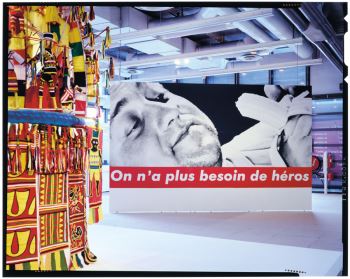 Installation view of Mike Chukwukelu's <i>Ijele (Prison)</i> (1989) and Barbara Kruger 's <i>On n'a plu besoin de héros (We Don't Need another Hero)</i> (1989) at the 1989 exhibition <i>Magiciens de la terre</i> at the Pompidou Centre