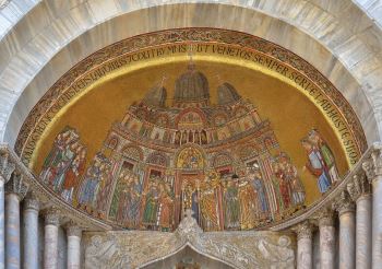 This photograph shows a mosaic, made of brightly color bits of stone, and a gold leaf background, above the entrance to San Marco in Venice.